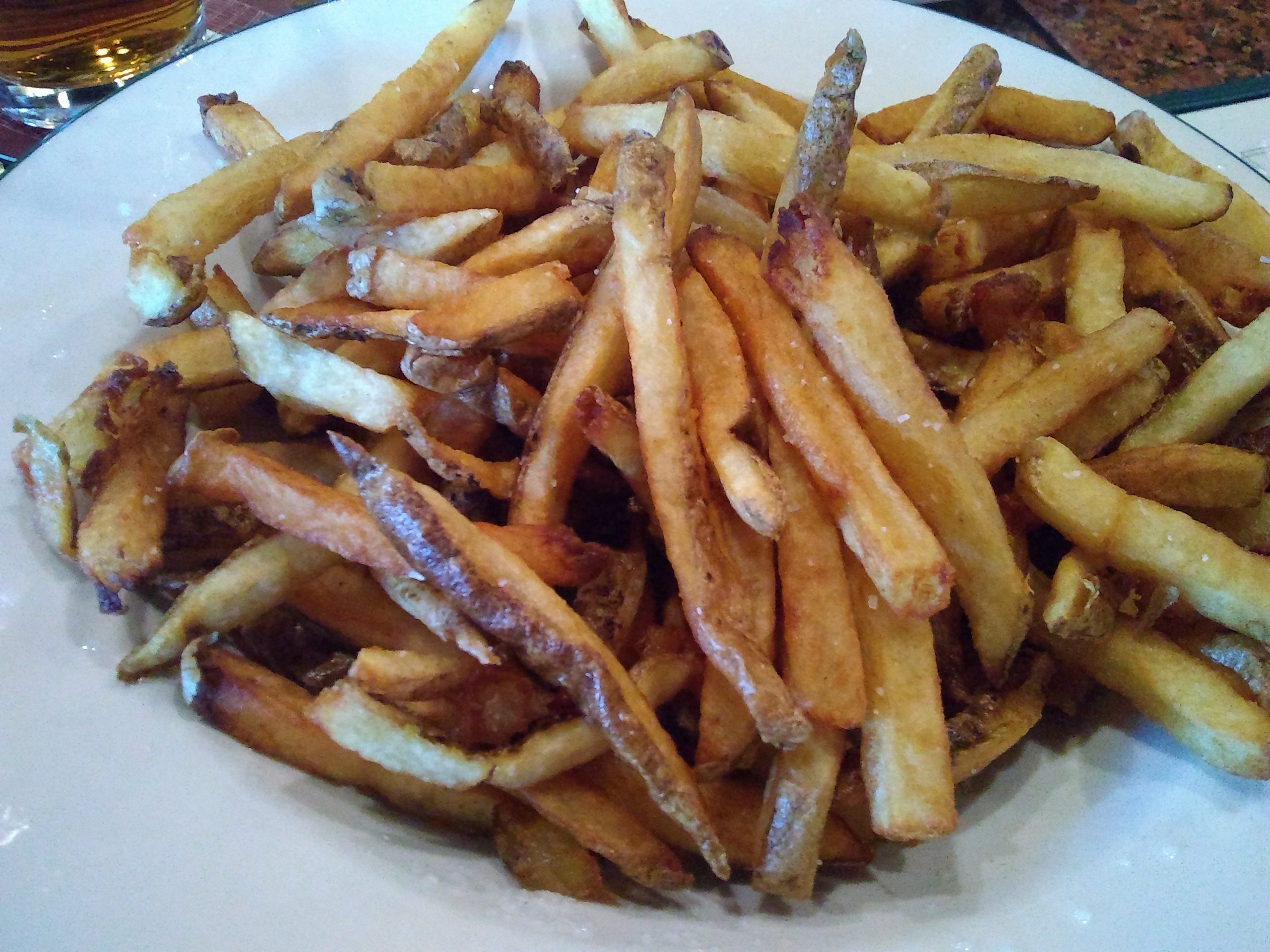 A plate of french fries with a glass of beer.
