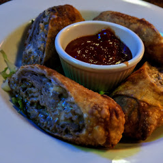 A plate of meat and vegetable spring rolls with dipping sauce.
