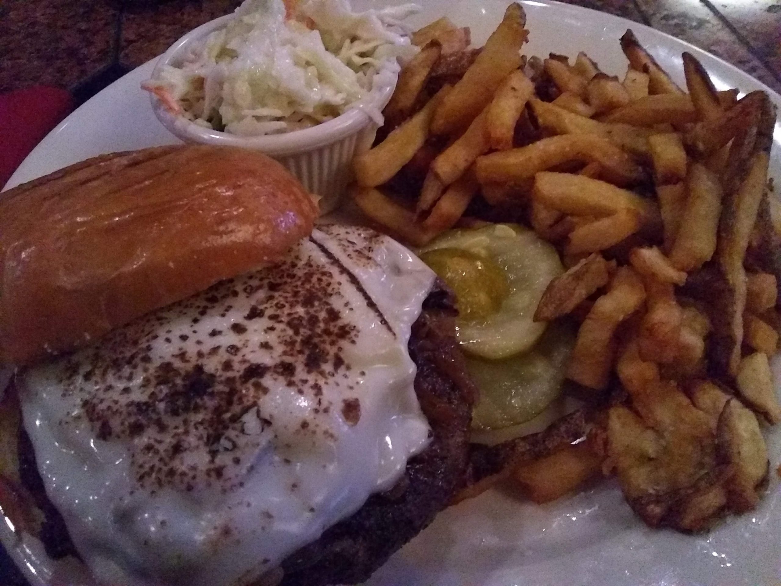 A burger with fries and coleslaw on a plate.