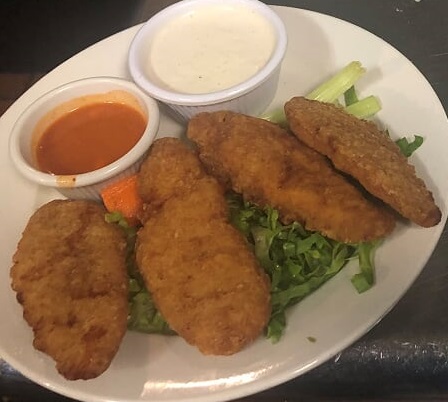 A plate with chicken fingers and a side of dipping sauce.
