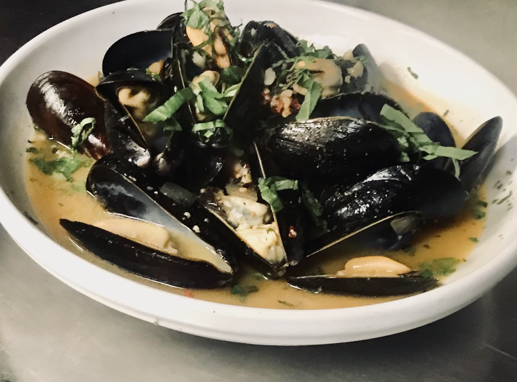 Mussels in a white bowl on a table.