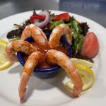 Shrimp on a plate with a salad and lemon wedges.