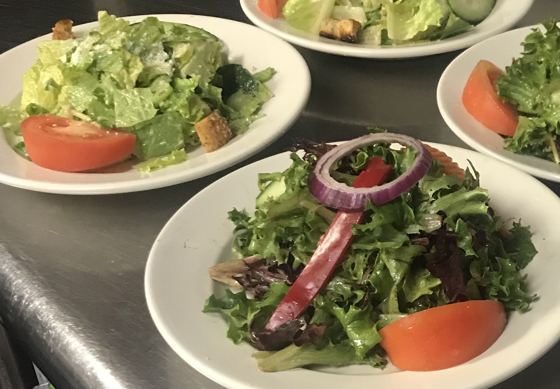 Four plates of salads on a table.